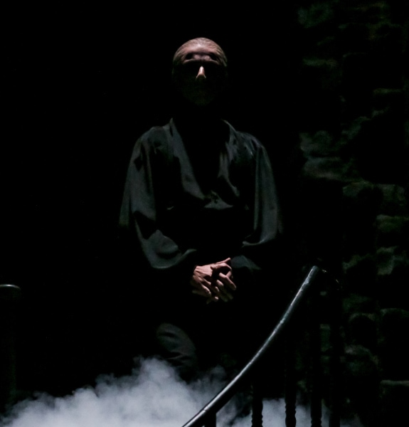 Davit Hovhannisyan, as Dracula, stands in dark shadow while dressed in all black