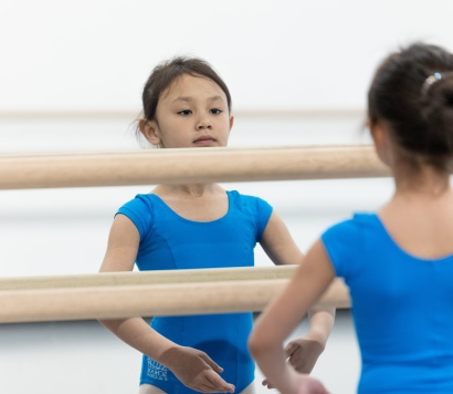 a child in blue leotard standing in front of a mirror