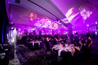 A room full of tables and guests with pink purple lighting covering the walls and ceiling