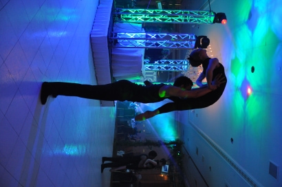 a man lifting a woman above his head, while performing under purple and green lights
