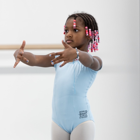 a child wearing ballet clothes and standing in first position