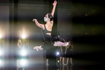 a girl in a black dress and white mask, leaping in the air