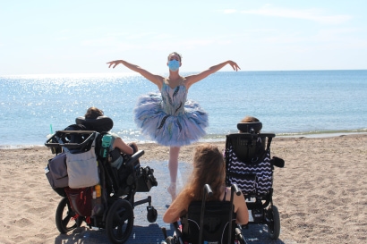 a ballerina dancing for two people in wheel chairs, on the beach