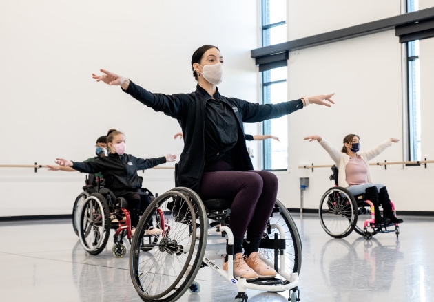a group of people in wheelchairs with masks, dancing in the studio