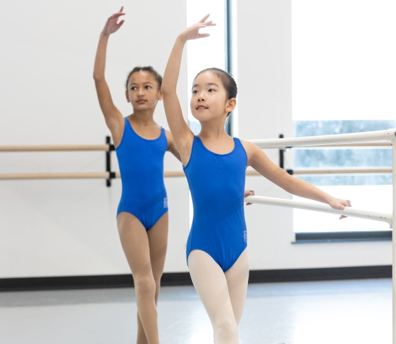 two young students working at the barre, in their blue ballet uniform